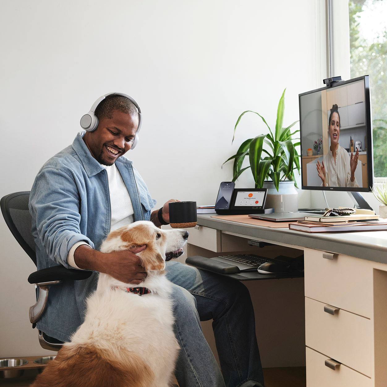 A person wearing headphones, petting their dog, sitting at a desk with a screen showing a Webex meeting.